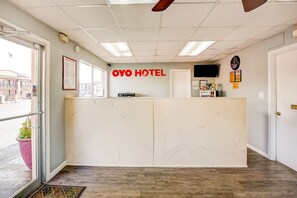 Un hall d’hôtel avec un comptoir de réception en marbre, une horloge et un téléviseur fixé au mur.