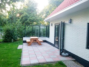 A patio with a wooden table and chairs, a glass door, and a white brick wall. - Park Retreat With Fireplace (Koudekerke)