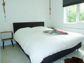 A bed with white bedding, a dark headboard, a bedside table, and a window with a view of greenery. - Park Retreat With Fireplace (Koudekerke)
