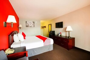 Habitación de hotel con cama, mesita de noche, lámpara, cómoda, televisor y un cuadro en la pared.