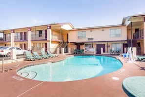 A hotel with a swimming pool, outdoor seating, and a two-story building.