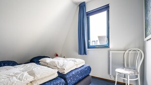 A room with two beds, a chair, a window with curtains, and a radiator. - Home With Dune Views in Zeeland (Vlissingen)