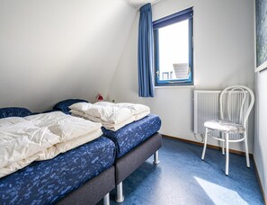 Ein Zimmer mit zwei Betten, einem Sessel, einem Fenster mit Vorhängen und einer Heizung.