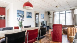 A modern dining area with a wooden table, red and black chairs, a potted plant, and maritime artwork on the walls. - Home With Dune Views in Zeeland (Vlissingen)