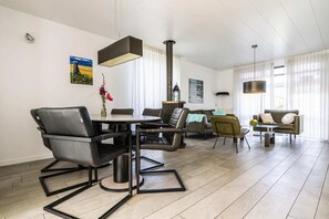 Ein modernes Wohnzimmer mit Essbereich, Kamin und großem Fenster mit transparenten Vorhängen.