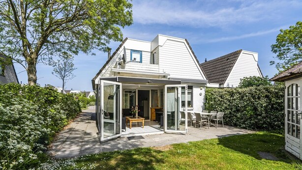 A modern house with a glass-enclosed patio, a lawn, and a large tree.