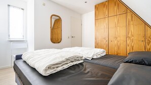 A bedroom with a bed, a wooden wardrobe, a mirror, and a window.