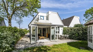A modern house with a glass-enclosed patio, a lawn, and a large tree.