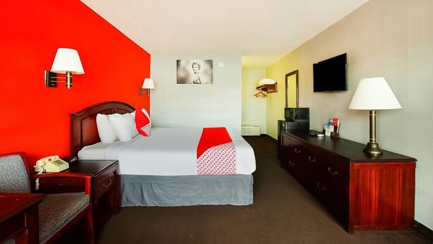 A hotel room with a bed, bedside tables, a desk, a chair, a television, and a wall-mounted TV.