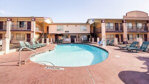 A hotel with a swimming pool, multiple balconies, and lounge chairs.