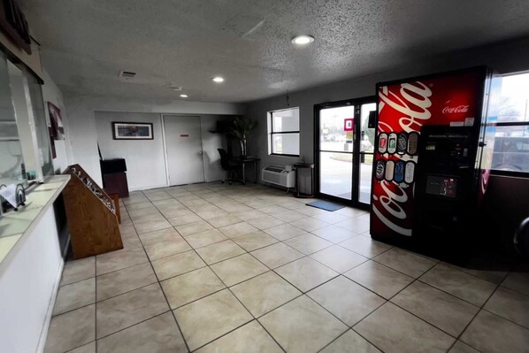A spacious room with a tiled floor, a Coca-Cola vending machine, a reception desk, and a window with a view of the parking lot.