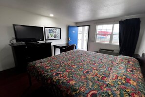 A hotel room with a bed, a desk with a computer, a television, and a window with curtains.