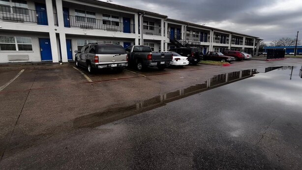 A multi-story motel with a row of parking spaces and a small pool area.