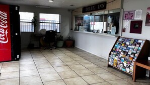 A hotel lobby with a Coca-Cola refrigerator, a reception desk, a window with blinds, and a bulletin board with various notices.