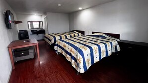 A hotel room with two beds, a desk, a television, and a small kitchenette.