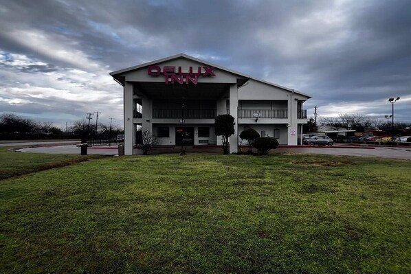 A DELUXE INN hotel with a flat roof, a covered entrance, and a parking lot.