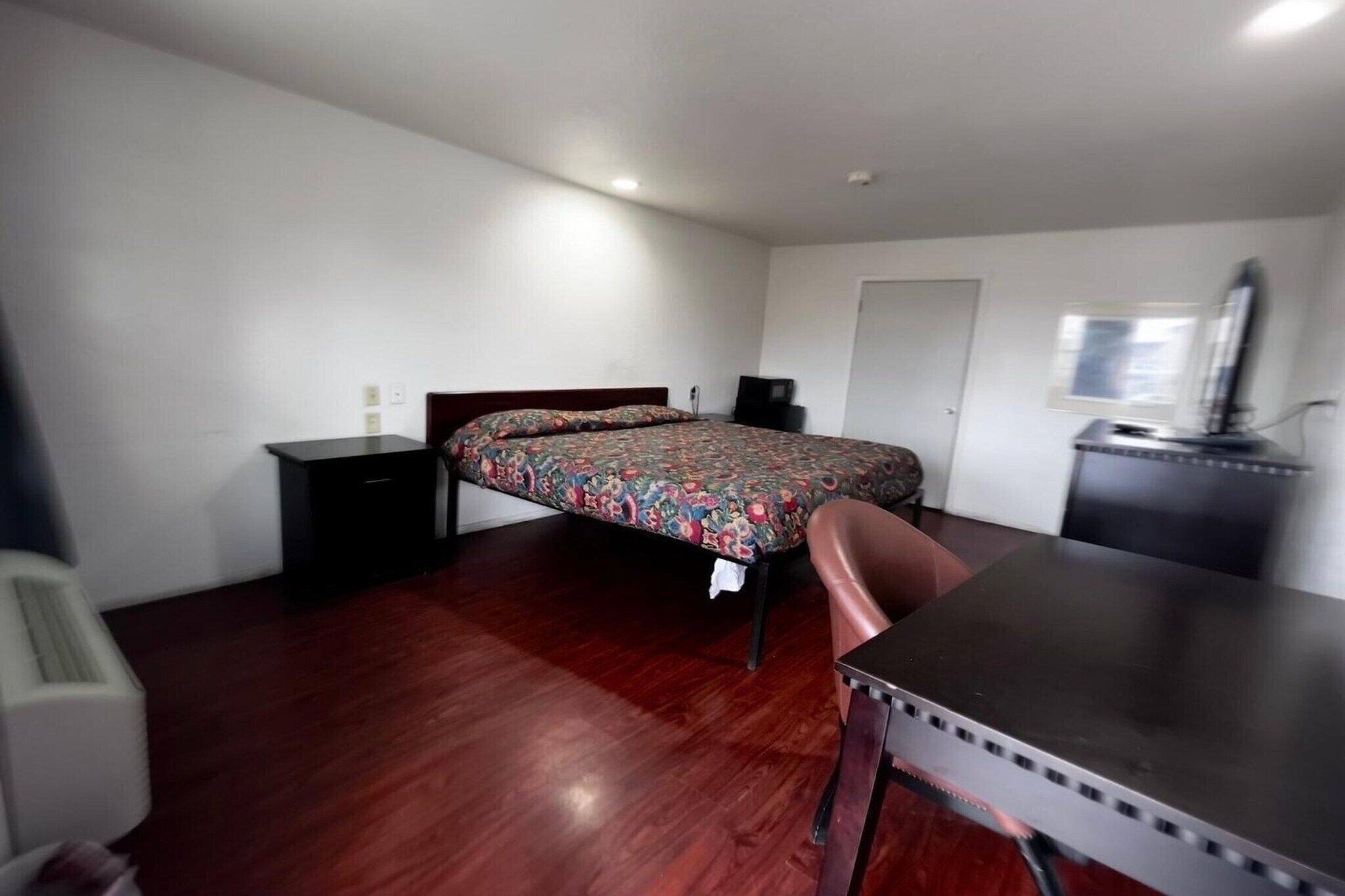 A bedroom with a bed, a desk, a chair, a dresser, and a television.