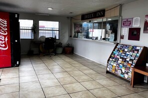 A hotel lobby with a Coca-Cola refrigerator, a reception desk, a window with blinds, and a bulletin board with various notices. - 2 Queen Beds Non-Smoking (Dallas)