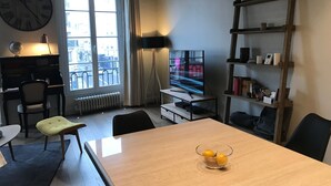 A living room with a wooden table, a TV, a bookshelf, a globe, and a window with curtains. - Charming high ceiling Le Marais St Paul apartment (Paris)