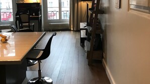 A room with a wooden floor, a large wall clock, a desk with a globe, and a window with curtains. - Charming high ceiling Le Marais St Paul apartment (Paris)