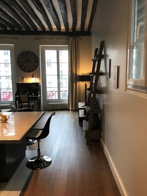 Ein Zimmer mit Holzboden, einer großen Wanduhr, einem Schreibtisch mit Globus und einem Fenster mit Vorhängen.