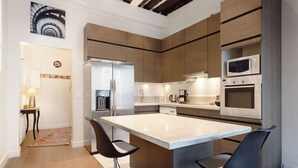 A modern kitchen with a central island, stainless steel appliances, and a dining area with two chairs. - Charming high ceiling Le Marais St Paul apartment (Paris)