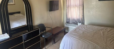 Una habitación de hotel con cama, escritorio, silla, televisor y ventana con cortinas.