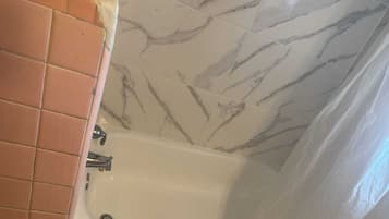 A bathroom with a bathtub, a tiled wall, and a corner with a different tile pattern.