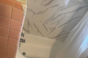 A bathroom with a bathtub, a tiled wall, and a corner with a different tile pattern. - Queen Bed|Smoking|Dallas (Dallas)