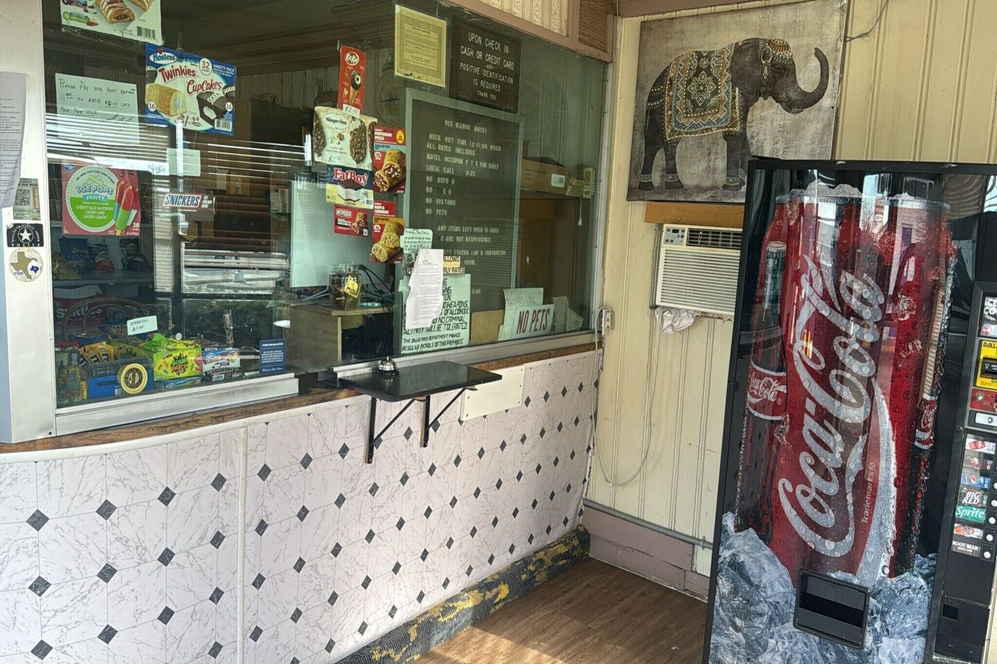 A snack bar with a Coca-Cola vending machine, a window display of snacks, and a sign prohibiting pets.