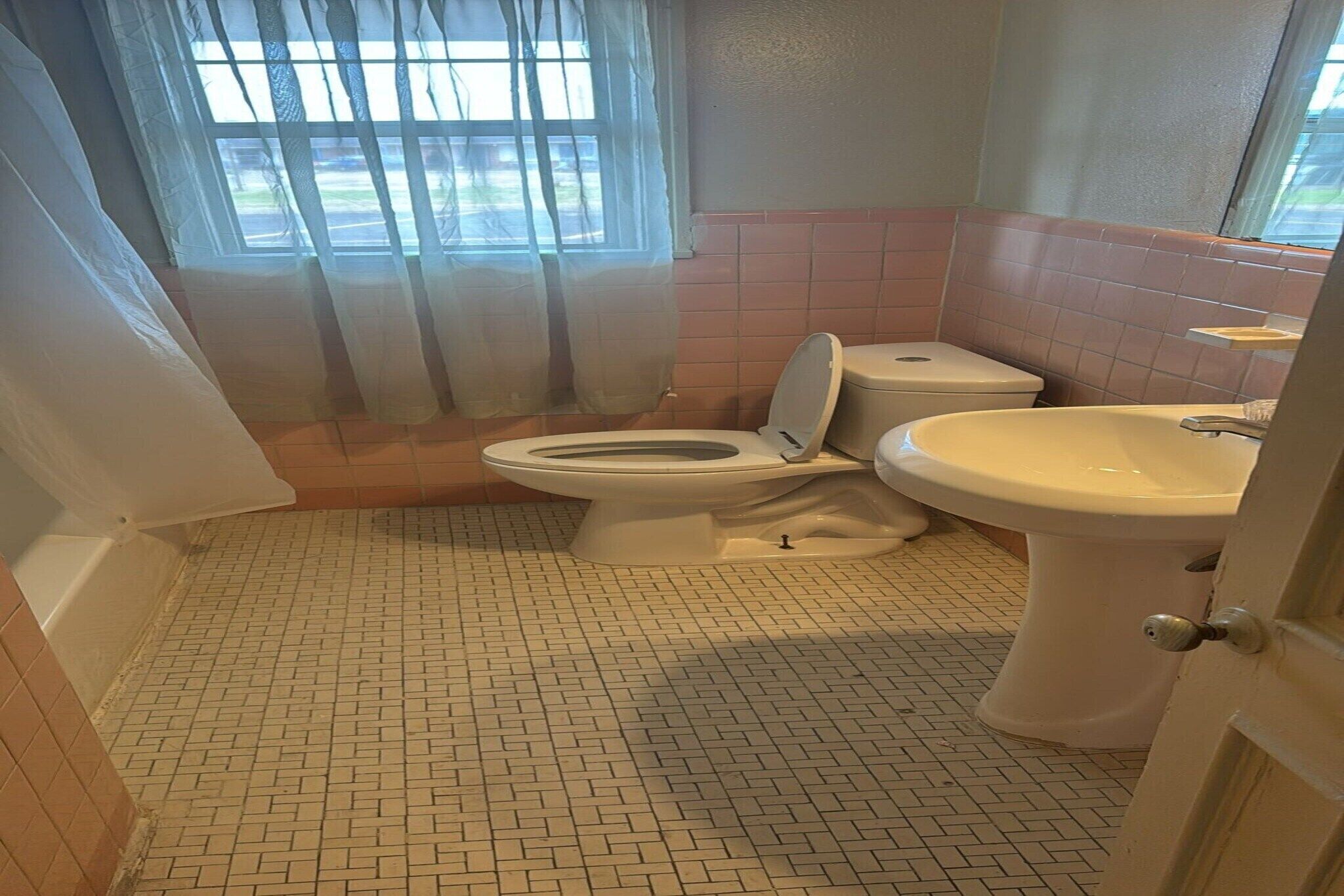 Een badkamer met toilet, wastafel en raam met gordijnen.