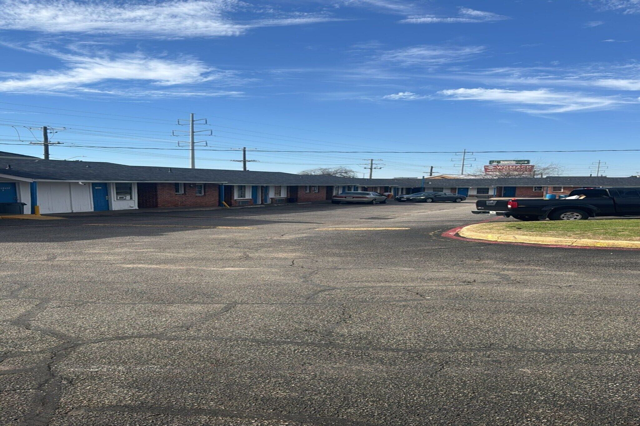 A motel with multiple rooms, a parking lot, and a building in the background.