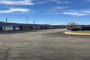 A motel with multiple rooms, a parking lot, and a building in the background. - Queen Bed Non-Smoking (Dallas)