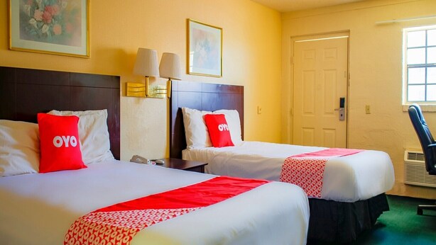 Habitación de hotel con dos camas, cada una con almohada roja de 'OYO', cabecero, lámparas de noche y ventana.