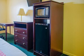 A hotel room with a bed, a desk, a dresser, a microwave, and a television.