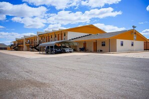 Un edificio con varios pisos, una zona de estacionamiento techada y un cielo despejado.