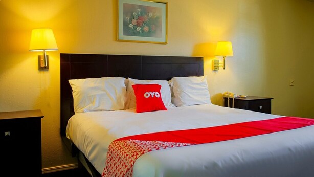 A hotel room with a bed, two bedside lamps, a nightstand, a telephone, and a framed picture on the wall.