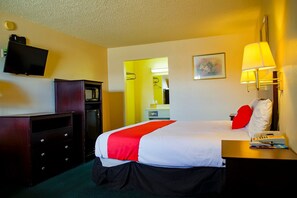 Ein Hotelzimmer mit Bett, Schreibtisch, Lampe, Telefon, Fernseher und Kleiderschrank.