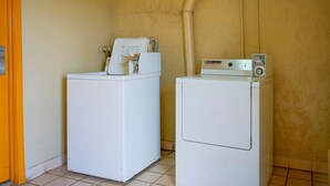Two white washing machines in a room with a tiled floor and a yellow wall.