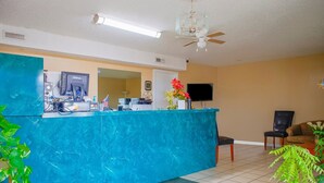 A reception area with a blue counter, a ceiling fan, a flat-screen TV, and a seating area with chairs.