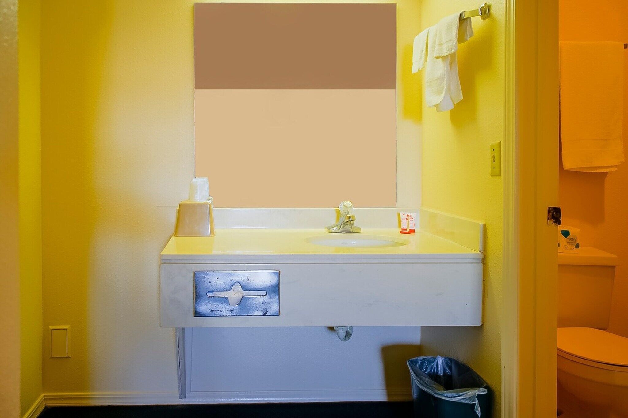 Een badkamer met een gele wand, een witte wastafel, een spiegel, een handdoekhouder en een toilet.