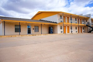Un motel de dos pisos con toldo amarillo, una recepción y una escalera visible al nivel superior.