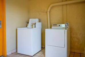 Dos lavadoras blancas en una habitación con piso de baldosas y pared amarilla.