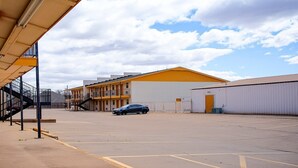 A parking lot with a building in the background, a car parked, and a staircase leading to a balcony.
