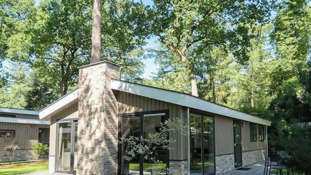 Een modern huis met een grote schoorsteen, grote ramen en een verzorgd gazon.