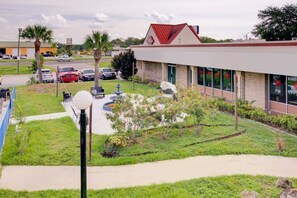 A building with a red roof, a parking lot, and a landscaped garden area with a fountain. - Queen Bed Non Smoking|Dundee (Dundee FL)