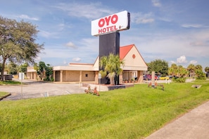 A hotel with a prominent sign, a parking lot, and a grassy area with a palm tree.