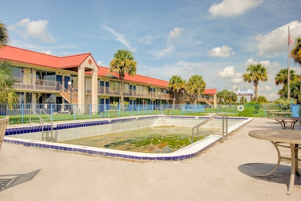 A hotel with a swimming pool, a covered outdoor area, and a flagpole.