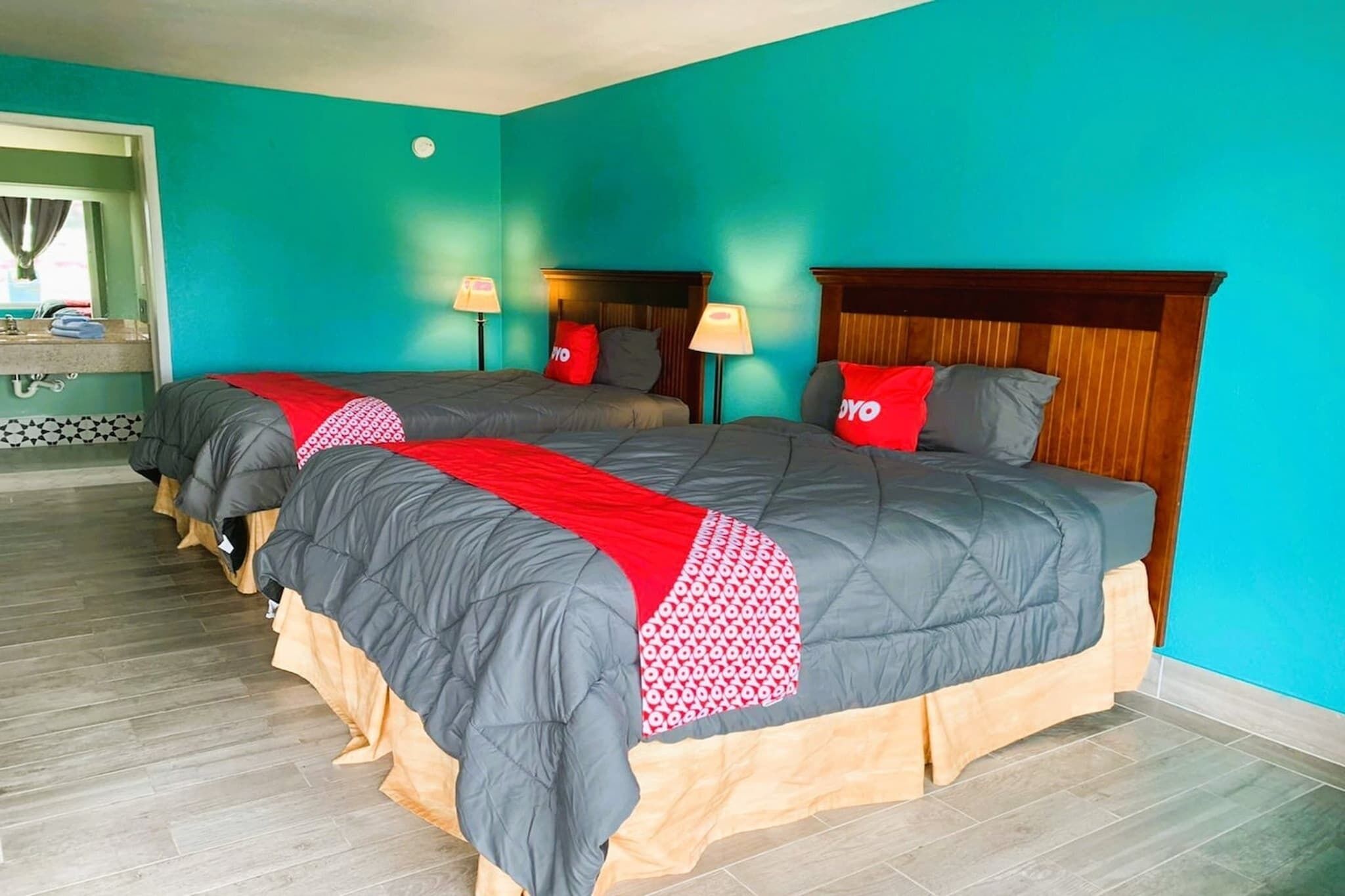 A hotel room with two beds, teal walls, wooden headboards, and a small window.