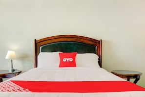 Ett hotellrum med en sänggavel i trä, en röd kudde med texten ”OYO”, ett vitt överkast och en röd- och vitrandig pläd.